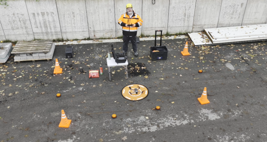 “Drohnenpilot in gesicherter Sicherheitszone mit Absperrkonen, Startplatz und Vermessungstechnik für professionelle Industrievermessung.
